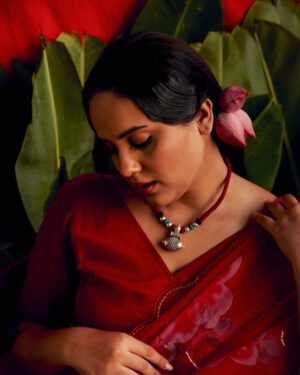 Woman wearing a Tribal style silver amulet necklace with red thread. Woman in the picture is dressed in red saree and lotus flower in the hair