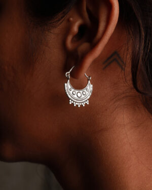 An woman wearing tribal designed silver hoop on the left ear. Small double arrow can be seen in behind the ear